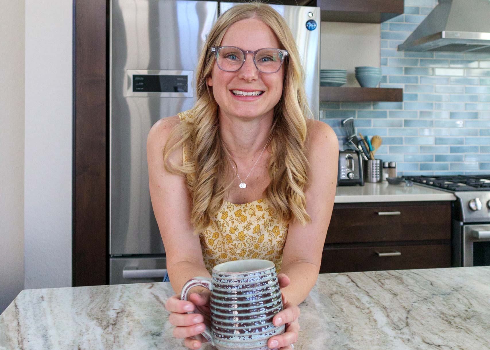 Functional and Integrative Medicine Provider Alison Percowycz, MSN, FNP-C smiling with a ceramic mug in her hand and a kitchen in the background in Denver Colorado