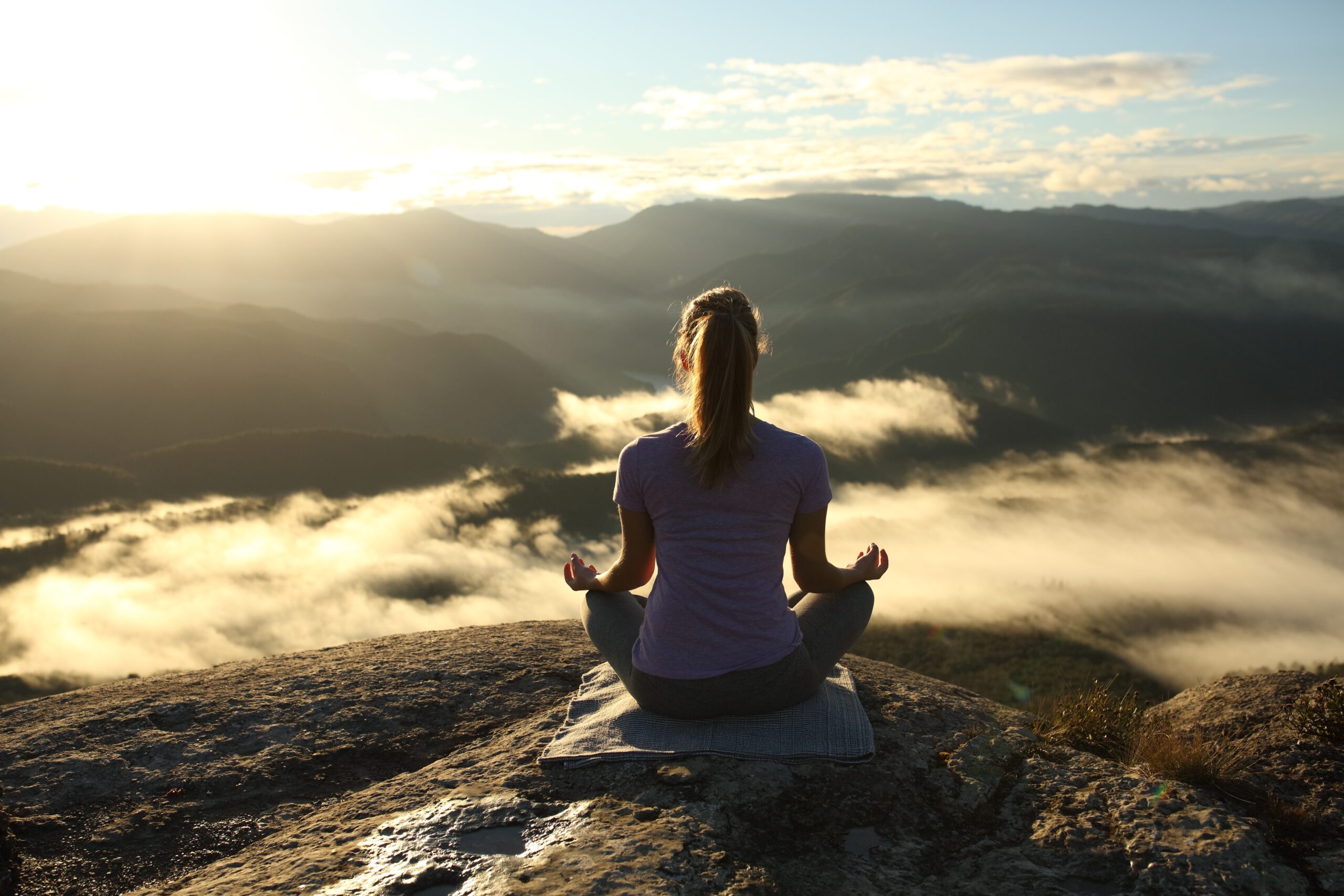 a woman meditating cross legged on a mountain top
